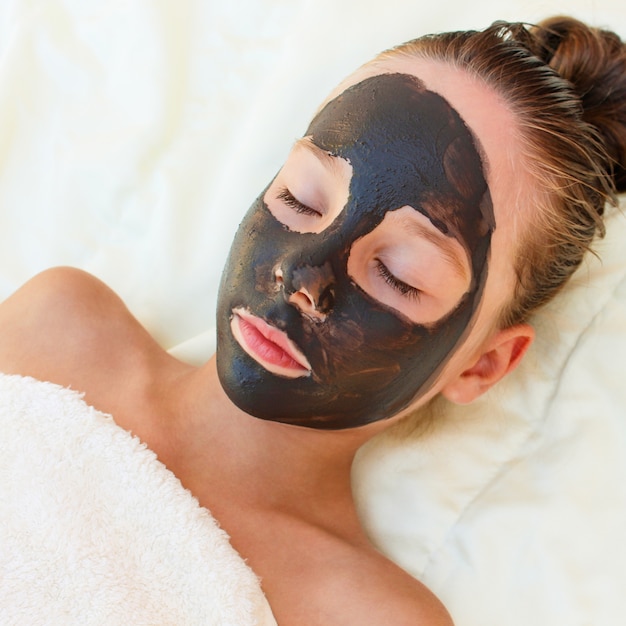 Beautiful girl with facial black clay mask.