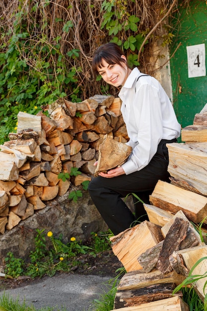 Фото Красивая девушка с дровами в белой рубашке в черных брюках с подтяжками вблизи