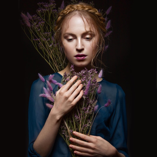 Bella ragazza con un'acconciatura da trucco delicata a forma di trecce vestito blu fiori secchi