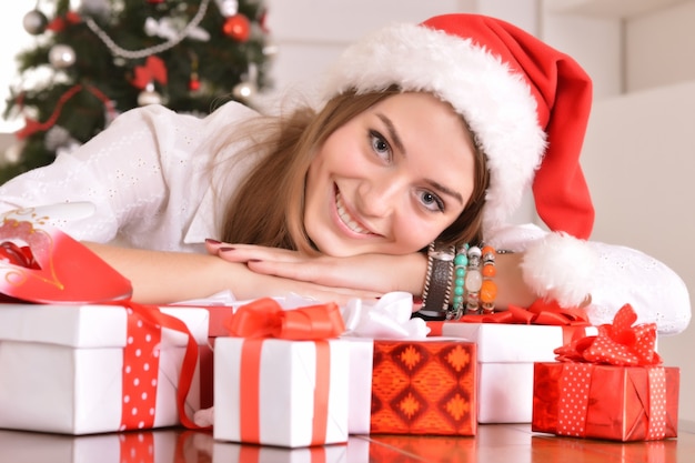 Beautiful girl with  gifts near the Christmas tree in santa hat