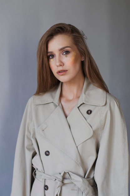 Beautiful girl with gold makeup with glitter and gold stars under eyes in trench coat