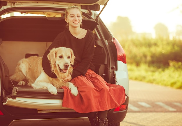 写真 美しい女の子とゴールデン・レトリバーの犬が 車のトランクに座って 笑顔で可愛いティーンエイジャーを抱きしめています