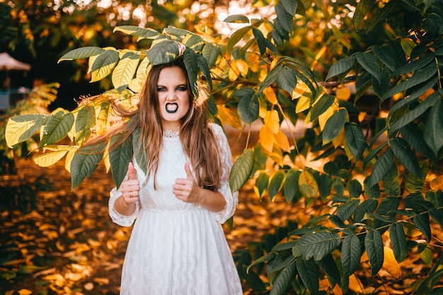 Beautiful girl with gothic make up and funny face expression posing in summer park.