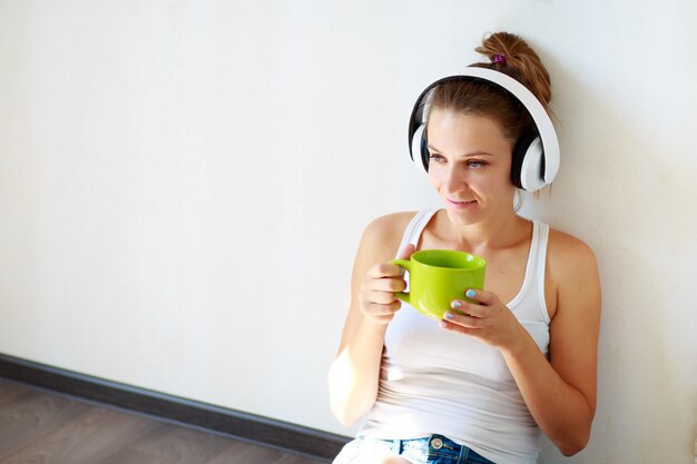 Beautiful girl with headphones listening to music and drinking coffee 