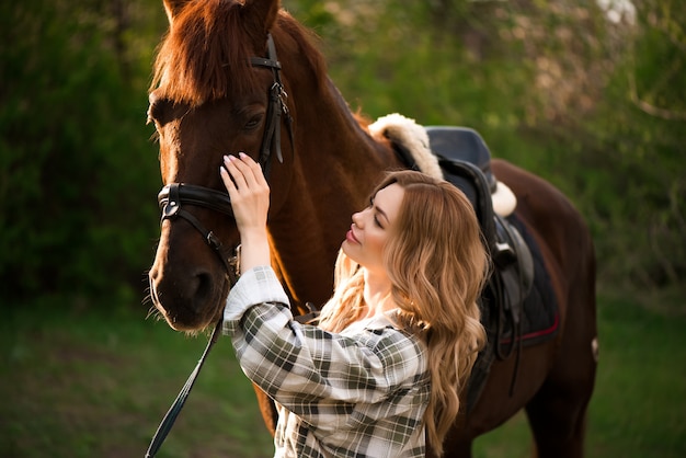 beautiful girl with her horse and beautiful warm sunset in the spring forest.