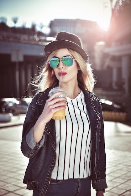 Beautiful girl with juice in sunglass walking at the street on urban style