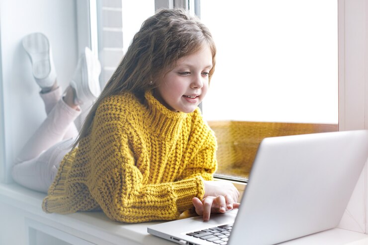Photo a beautiful girl with a laptop at home at the window looks at the screen and smiles. the girl at home communicates on the internet. kids distance learning.