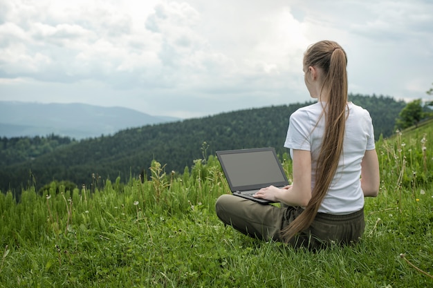 Beautiful girl with a laptop sitting on green grass