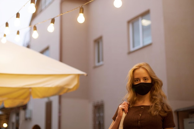 Beautiful girl with light hair in a black medical mask walking in the street