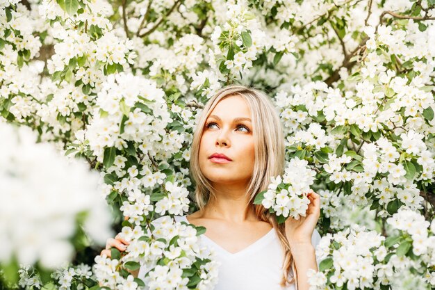 Foto bella ragazza con capelli chiari, vetri, vicino ad alberi di fioritura, melo, molla, rami, fiore, moda, stile, europeo, rosso