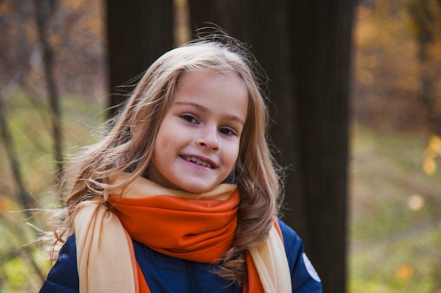 Bella ragazza con lunghi capelli biondi nel parco autunnale. ragazza dagli occhi marroni con trecce dorate su uno sfondo di foglie autunnali gialle