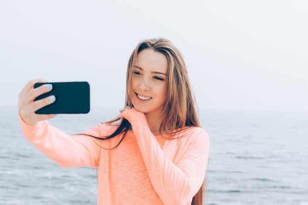 Beautiful girl with long brown hair takes pictures of herself on the phone at the beach