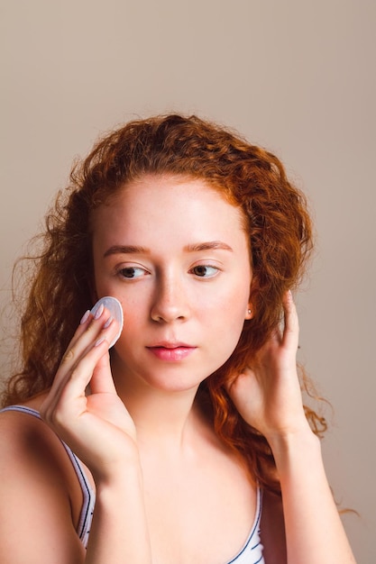 Beautiful girl with long curly hair In hand a cotton pad wipes his face Young Skin Care Concept