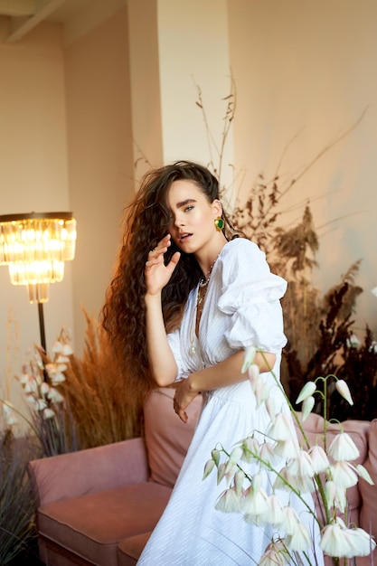 A beautiful girl with long curly hair in a white long dress is moving dynamically Photo studio with cereals Fashion and beauty