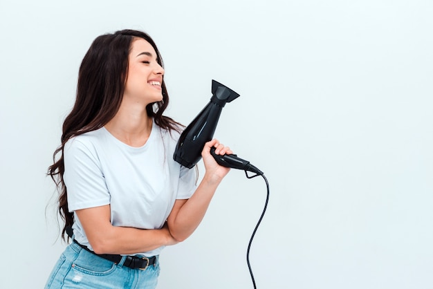 Bella ragazza con lunghi capelli scuri tiene un asciugacapelli