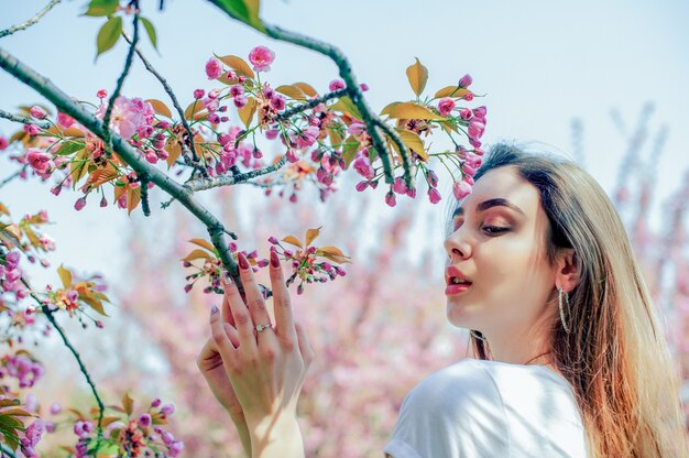 長い髪の美しい少女は、開花する桜の木の近くで春の自然の美しさを楽しんでいます。