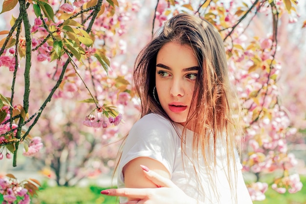 Beautiful girl with long hair enjoys the beauty of spring nature near the blossoming sakura tree.