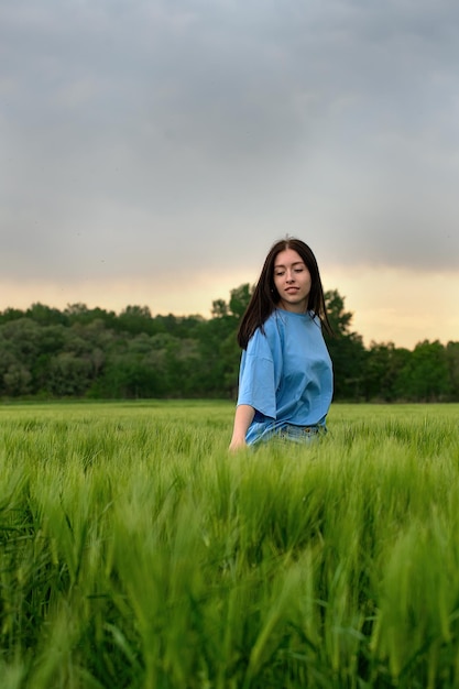 A beautiful girl with long hair enjoys life and nature in a bright green wheat field in spring