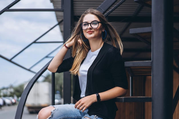 Beautiful girl with long hair and glasses sitting on metal stairs