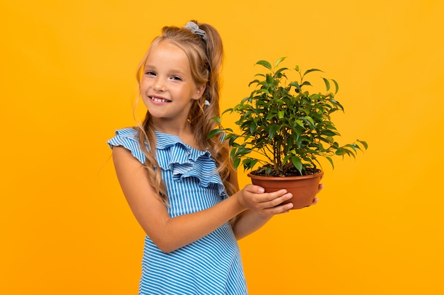 Beautiful girl with long hair holds a plant and smiles, picture isolated on yellow