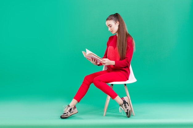 Bella ragazza con i capelli lunghi in maglione rosso legge il libro. copia spazio