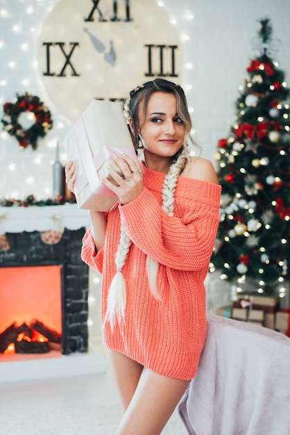 Photo beautiful girl with naked sexy legs in a sweater holding a gift box near her ear cool