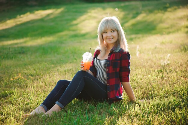Bella ragazza con un cocktail arancione sull'erba nel parco