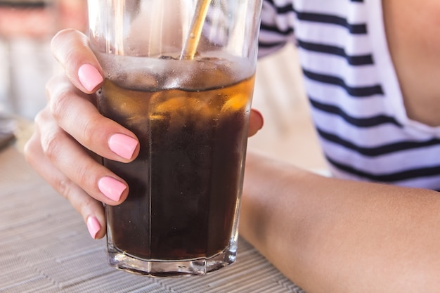 La bella ragazza con un manicure rosa tiene e bevendo un grande vetro con soda