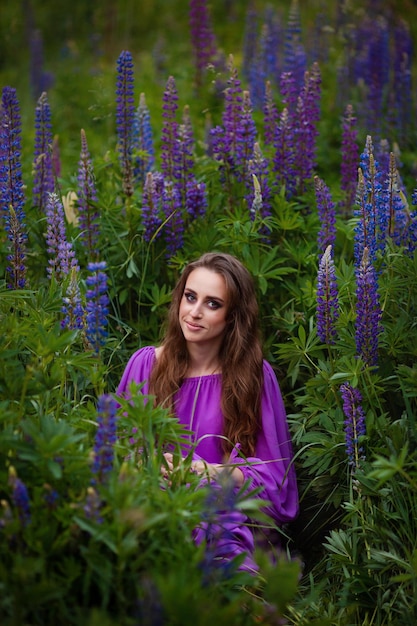 Beautiful girl with professional makeup in purple dress sitting in lupine flowers