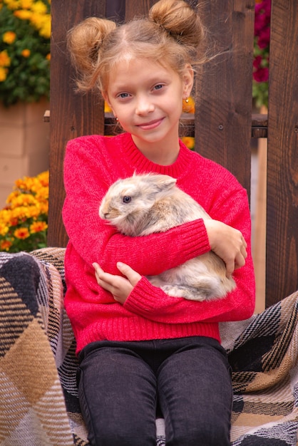 beautiful girl with a rabbit outdoors in autumn near the house on the bench
