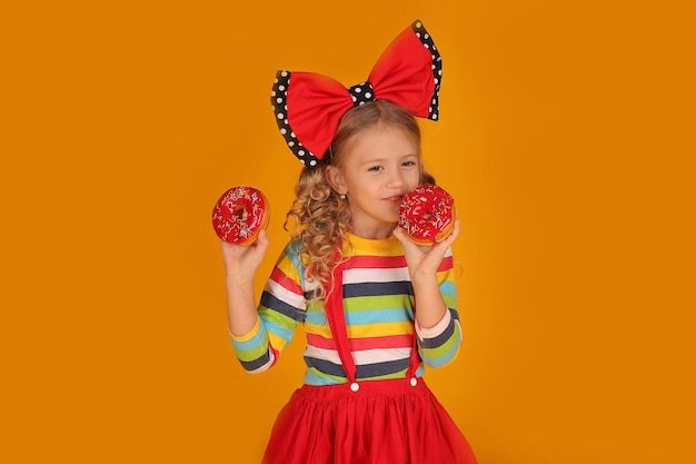 beautiful girl with a red bow on her head in a red skirt a colored blouse holds pink donuts