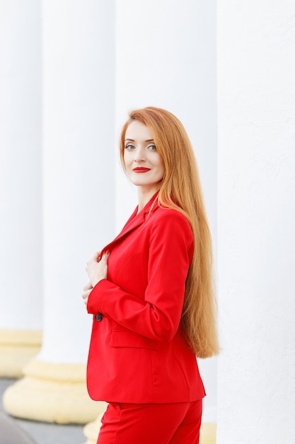 Beautiful girl with red hair dressed in a red business suit Business portrait