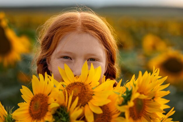 Beautiful girl with red hair and freckles stands in a field with sunflowers