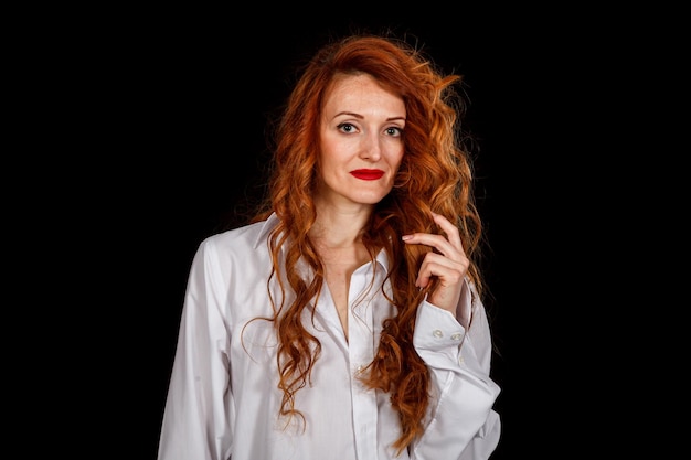 Photo beautiful girl with red hair in a white shirt and a hat on a black background