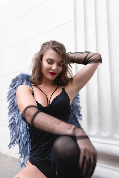 Beautiful girl with red lips in a black bodysuit gloves and blue wings Posing looking at the camera