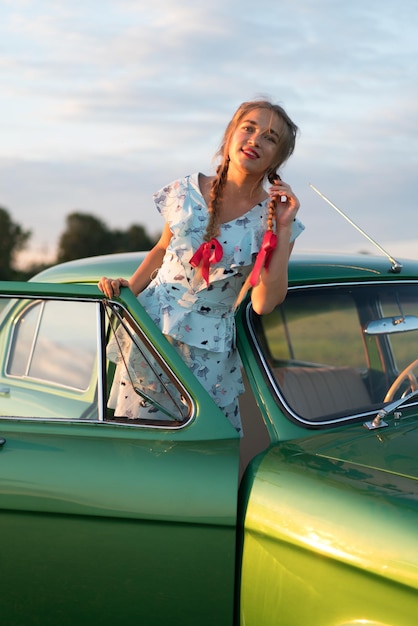 写真 教会と有名なロシアの車volgaのあるフィールドで赤いリボンを持つ美しい少女