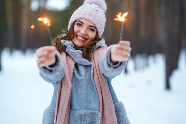 Beautiful girl with sparklers in hands. The girl is dressed in a blue coat, in a light knitted hat, scarf and mittens.
