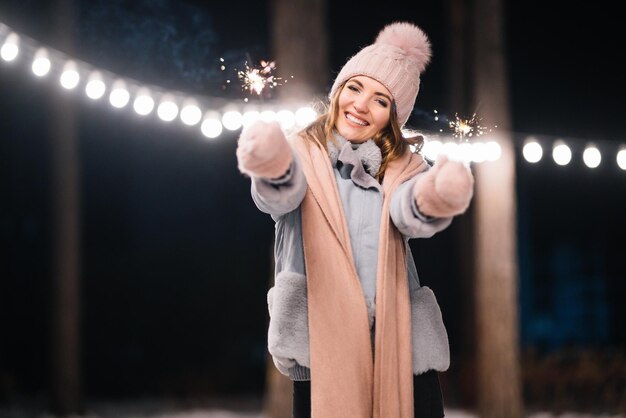 手で線香花火を持つ美しい少女 森で幸せな冬の時間 お祝いガーランド ライト。クリスマス