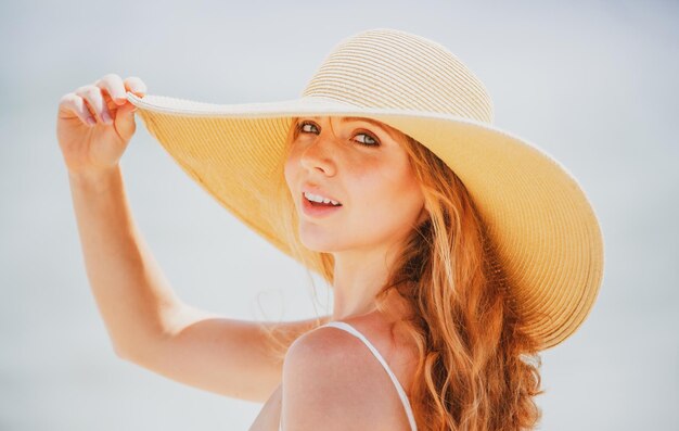 Beautiful girl with straw hat enjoying sunbath at beach Young tanned woman enjoying breeze at seaside Carefree woman smiling with sea ocean in background