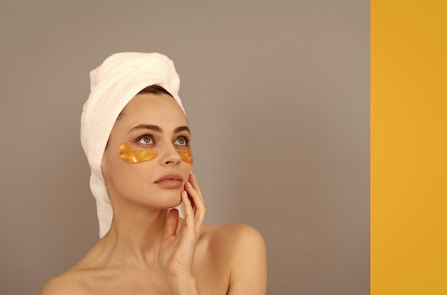 Beautiful girl with terry towel use facial golden eye patch for skin copy space beauty