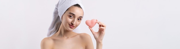 Beautiful girl with thick eyebrows and perfect skin at white background towel on head beauty photo Holding a cosmetic pink heart sponge