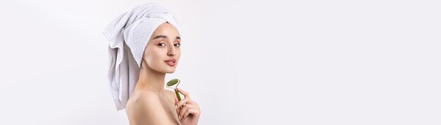 Beautiful girl with thick eyebrows and perfect skin at white background towel on head beauty photo Holds a cosmetic roller