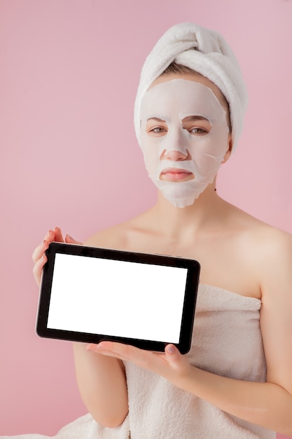 Beautiful girl with a tissue mask and a tablet in their hands with copy space on a pink space