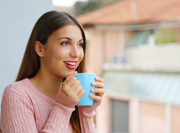 朝は温かい飲み物を楽しむ暖かいセーターで美しい少女