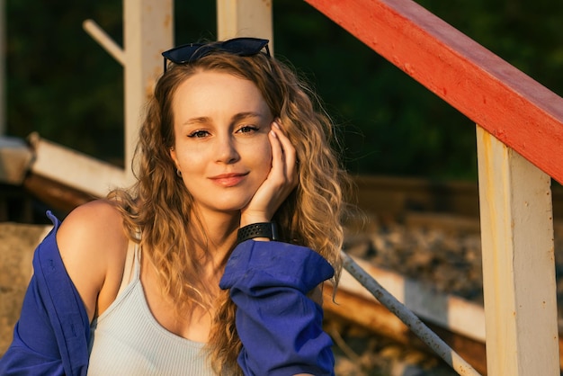 Beautiful girl with wavy hair in the rays of the setting sun on the background of the railway