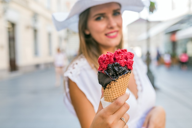 Beautiful girl with white hat eating ice cream on city street