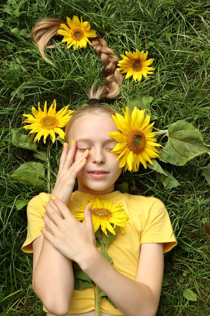 A beautiful girl with a yellow manicure lies on the grass with sunflowers