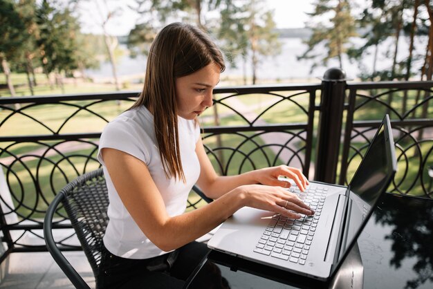 A beautiful girl works with her laptop on the balcony on a summer day.