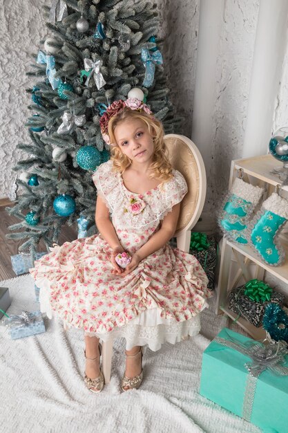 Beautiful girl in a wreath and dress near Christmas tree