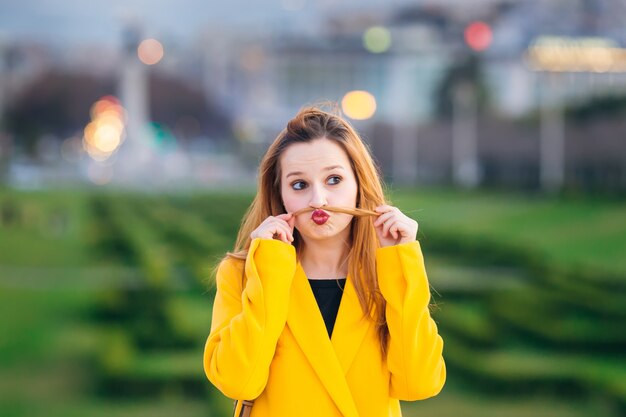 Una bella ragazza in un cappotto giallo mostra una smorfia. divertiti. cit